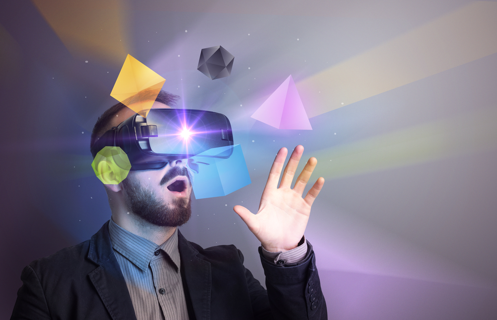 Ein Mann mit Virtual-Reality-Headset blickt fasziniert auf bunte, schwebende 3D-Objekte wie Würfel, Pyramiden und Polyeder, die ihn in einer virtuellen Umgebung umgeben.