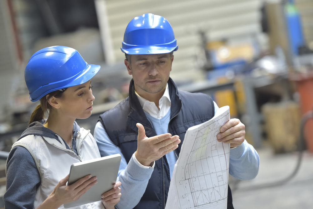 Ingenieure mit blauen Schutzhelmen in einer Maschinenfabrik lesen einen Bauplan