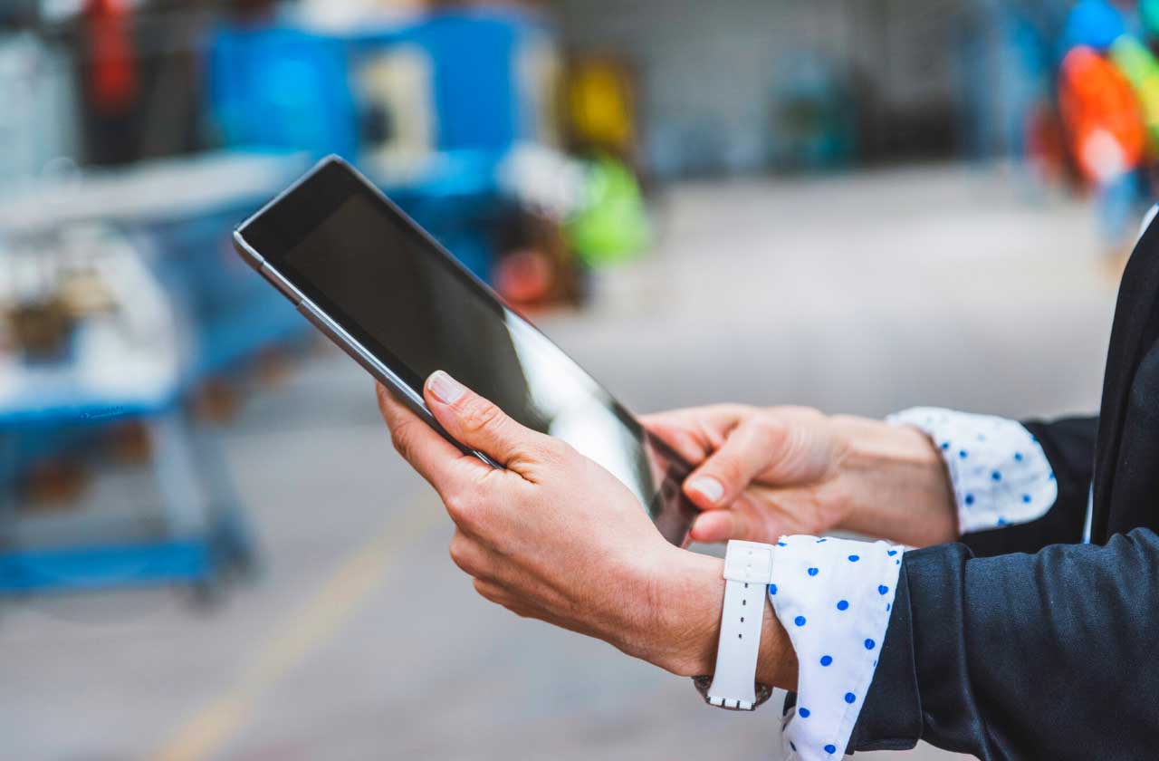 Digitale Projektsteuerung in der Industrie: Person hält Tablet zur Erfassung von Echtzeitdaten in der Fertigungshalle